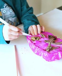 a young boy is eating something out of a pink bowl on the table with white chopsticks