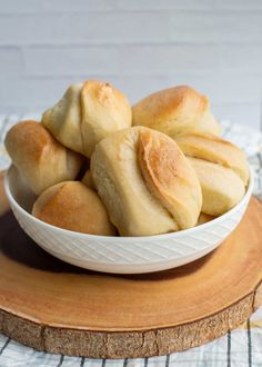 a white bowl filled with rolls on top of a wooden board