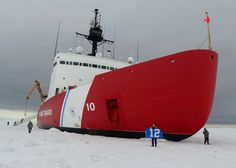 a large red and white boat sitting on top of snow covered ground next to people