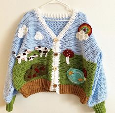 a knitted sweater with farm animals and mushrooms on the front is hanging from a hook