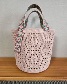 a pink crocheted bag with a green and red ribbon hanging from the handle