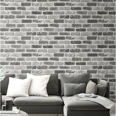 a couch sitting in front of a brick wall with pillows on top of it's back