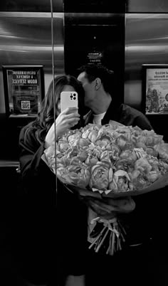 a man holding a bouquet of roses taking a selfie with his cell phone in front of him