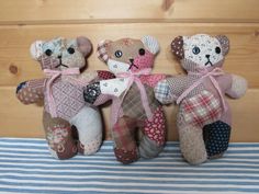 three stuffed teddy bears sitting on top of a blue and white striped bed sheet next to a wooden wall