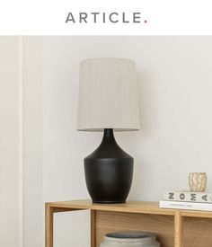 a black lamp sitting on top of a wooden table next to a white vase and book