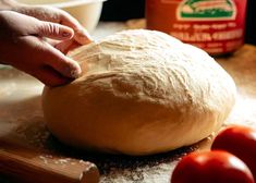 a person kneading dough on top of a wooden table next to some tomatoes