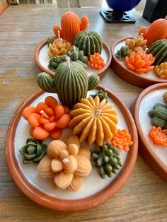 four plates with different types of vegetables on them sitting on a wooden table in front of a window