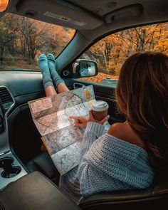 a woman sitting in the back seat of a car looking at a map and holding a cup