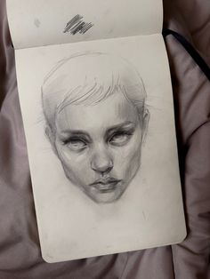 a pencil drawing of a woman's face on a piece of paper that is laying on a bed