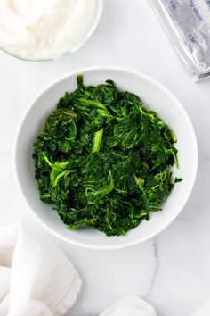 a white bowl filled with spinach next to a container of yogurt