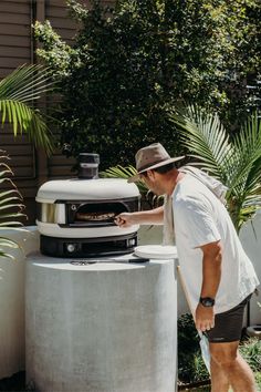 a man walking past an outdoor pizza oven in the backyard with palm trees behind him