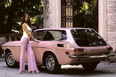 a woman standing next to a pink car