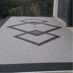 a black and white pattern is on the concrete outside an apartment building, with bushes in the background