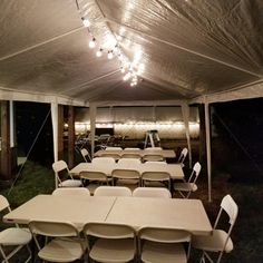 tables and chairs are set up under a large white tent with lights hanging from the ceiling