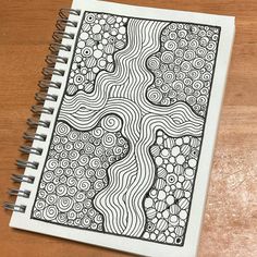 a spiral notebook with black and white designs on the cover sitting on a wooden table