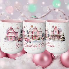 three coffee mugs with christmas scenes on them sitting in the snow next to pink ornaments