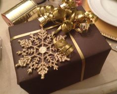 a present wrapped in brown paper with gold ribbon and snowflake decoration on top