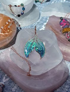 three pieces of jewelry are sitting on top of some ice cubes and one has a leaf shaped pendant hanging from it