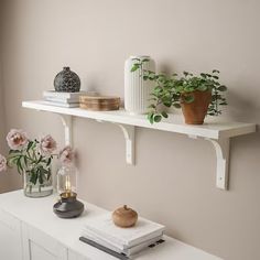 two white shelves with vases, books and flowers on them next to each other