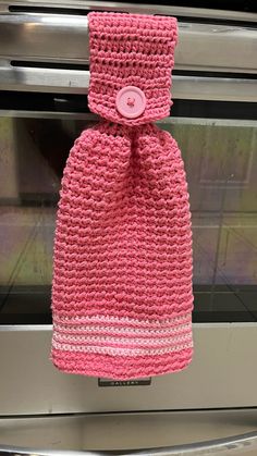 a pink crocheted bag hanging from the side of an oven door, with a button on it