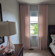 a bedroom with a bed, nightstand and pink drapes on the window sill