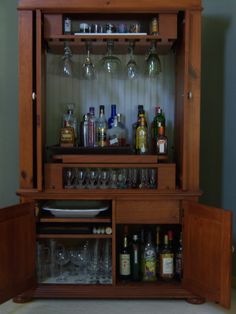 a wooden cabinet with wine glasses and liquor bottles on the top shelf in front of it