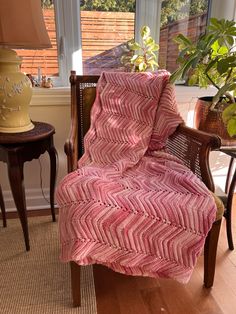 a chair with a pink blanket on top of it next to a lamp and potted plant