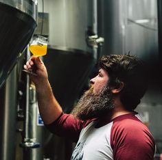 a man with a beard holding a glass in front of a brewery tank filled with beer