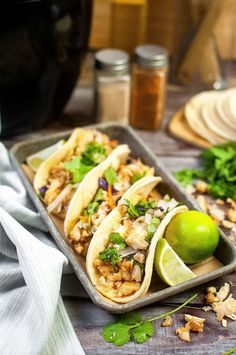 three tacos with limes and cilantro on a tray next to tortillas