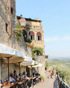 people are sitting at tables in front of an old stone building with windows and balconies