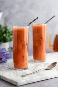 two glasses filled with liquid sitting on top of a marble tray next to a silver spoon