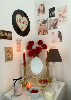 a white table topped with a mirror and red flowers next to a bowl of fruit