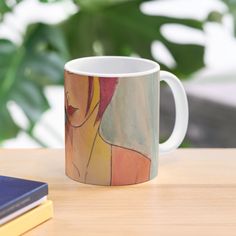 a coffee mug sitting on top of a wooden table next to a book and plant