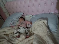 a small child laying on top of a bed covered in blankets and pillows with a pink headboard