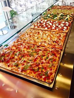 several pizzas are lined up on display in a glass case at a buffet table