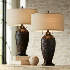 two lamps sitting on top of a table in front of a brick wall and window