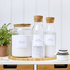 three jars with labels on them sitting on a shelf next to a potted plant