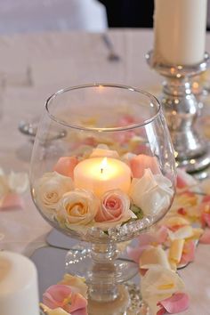 a candle that is sitting in a glass bowl on a table with flowers and candles