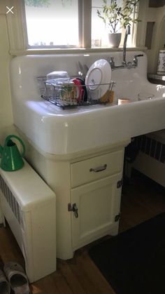 a white sink sitting under a window next to a green pot and pan on top of a counter