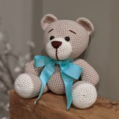 a crocheted teddy bear sitting on top of a wooden box with a blue ribbon