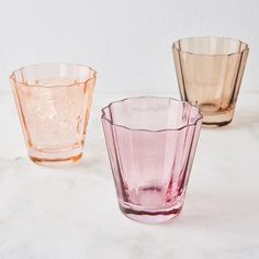 three different colored glass cups sitting on top of a white countertop next to each other