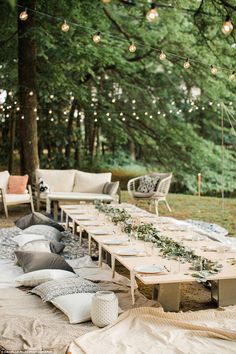 a long table with lots of pillows and lights hanging from the trees in the background