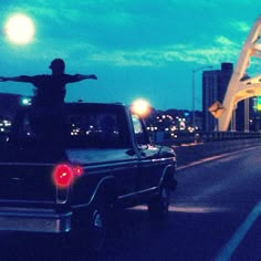 a man standing on the back of a pickup truck in front of a bridge at night