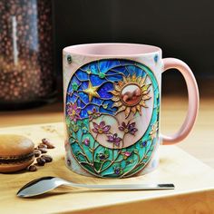 a pink coffee mug sitting on top of a wooden table next to a spoon and cup