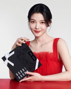 a woman in a red dress holding up a black box with the word bobbi brown on it