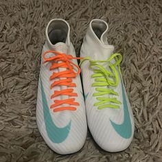 pair of white and blue shoes with neon orange laces on the soles sitting on carpet