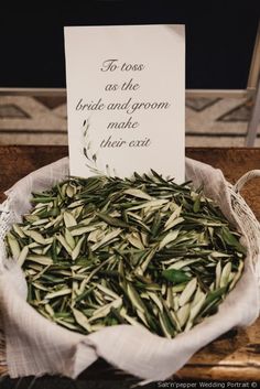 a bowl filled with green leaves next to a sign that says to toss as the bride and groom make their exit