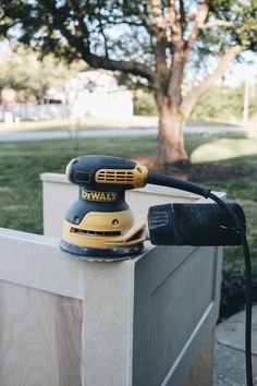 a corded sander sitting on top of a cement block next to a tree