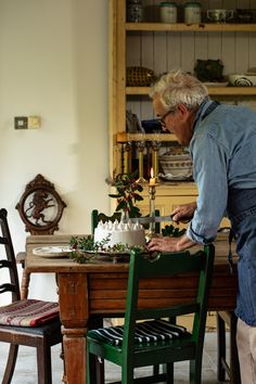 an older man is decorating a table with flowers and greenery in his home