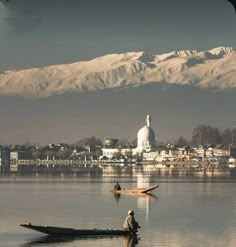 a man on a boat in the middle of a lake with mountains in the background